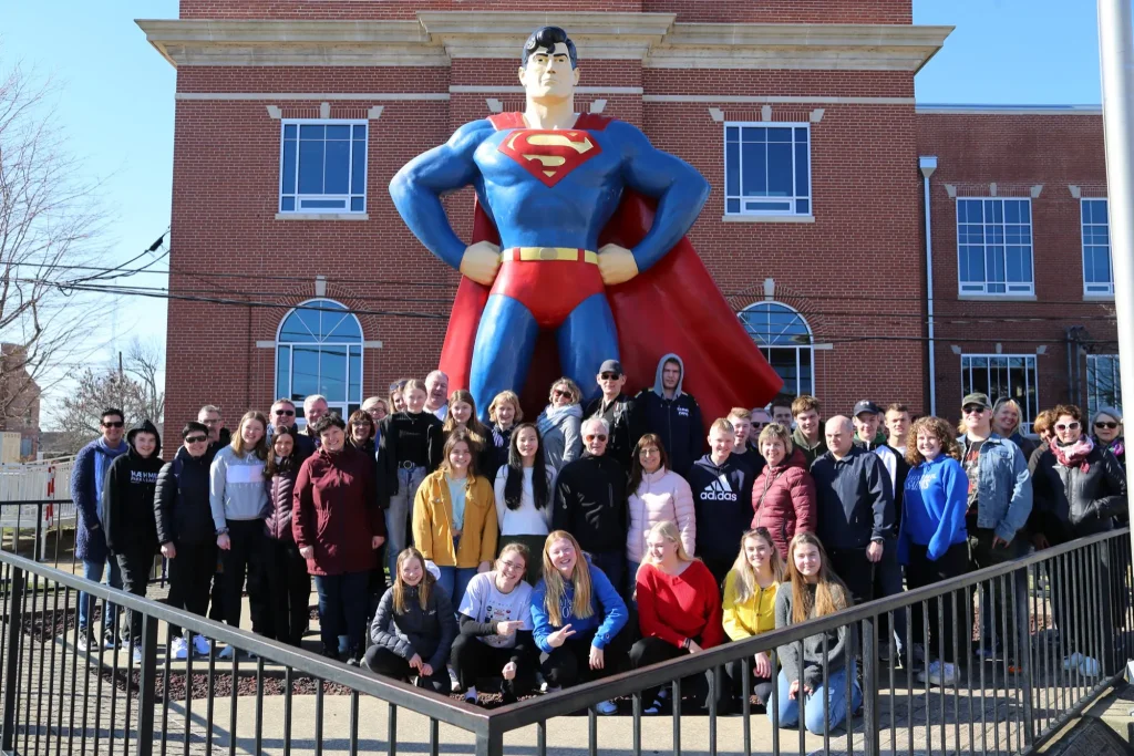 A large group poses in front of the Superman statue in Metropolis